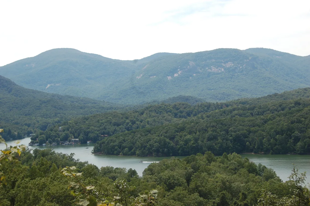 A breathtaking view of a mountain range with a river winding through lush forests, caught at sunset. The landscape is tranquil and immersive, ideal for hiking, boating, or nature photography. Wildlife observation is possible, and the beauty of the sunset paints the scene in warm, inviting tones.