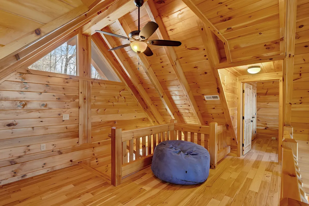 A bright, open space with a blue bean bag chair, wooden railing, angled wooden beams, and multiple windows. The atmosphere is warm and lively, suggesting a multipurpose family zone for reading, playing games, or gathering together.