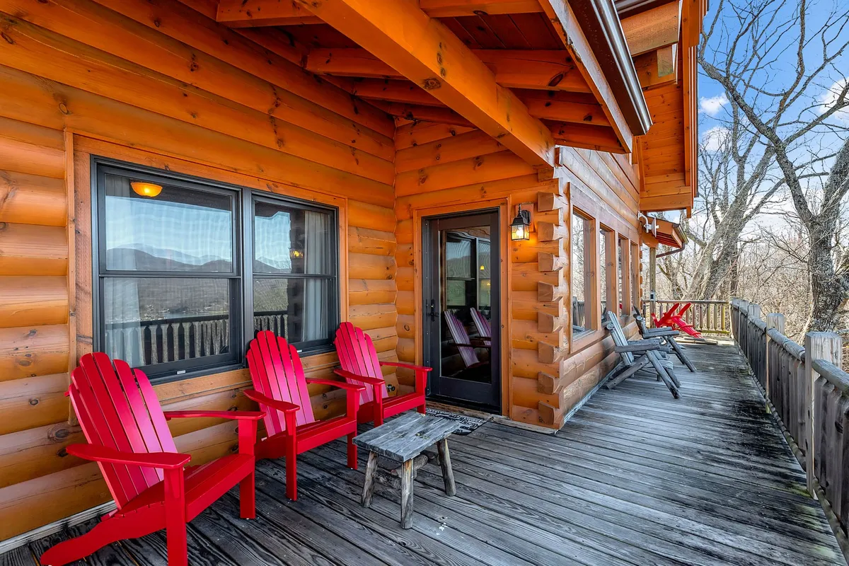 This image showcases a cozy wooden deck outfitted with red Adirondack chairs and large windows, set against a stunning mountain backdrop. The inviting arrangement encourages relaxation, socializing, and enjoying coffee while soaking up the expansive outdoor views.