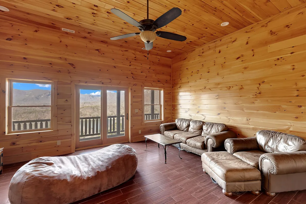 A spacious area featuring expansive windows, plush leather couches, an inviting bean bag chair, and warm wooden ceilings. The scene is set for both group gatherings and quiet moments—perfect for movie nights or relaxing with a book.