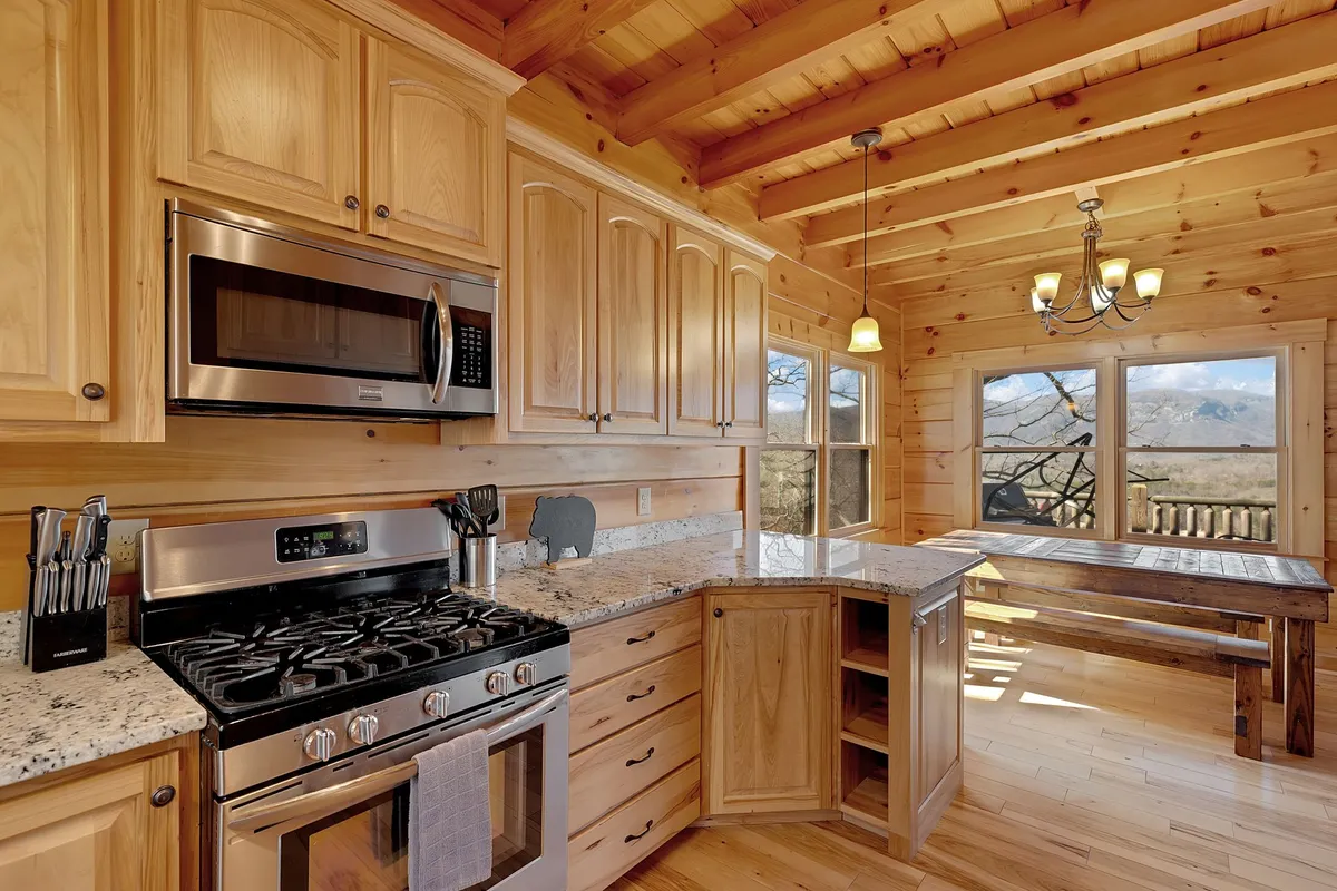 A spacious kitchen and dining area, with a granite countertop, modern stainless steel appliances, and a wooden dining table positioned to enjoy panoramic views out the window. The warm wood cabinetry and natural light create an inviting atmosphere for cooking and entertaining.