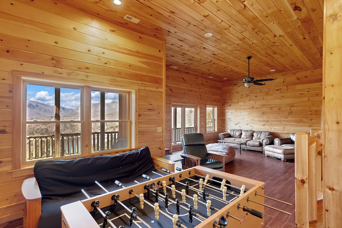 This image captures the heart of the basement family room, with a foosball table set up for friendly competition, leather couches inviting relaxation, and large windows that let in natural light. The open layout and cozy furnishings suggest a lively yet comfortable space for both play and unwinding.